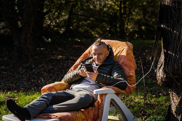 Photo a portable solar battery is hanging from a tree a man resting in nature with a mobile phone in his hands charging phone from solar eco energy