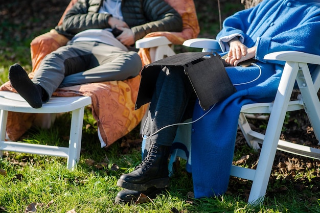 A portable solar panel rests on the legs of a woman talking to a man Camping Ecological alternative energy concept