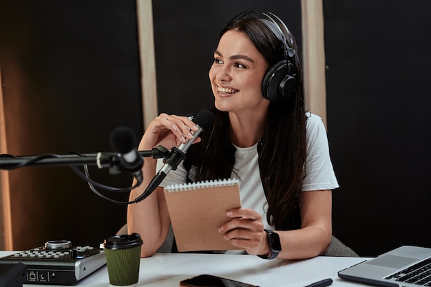 Portait of attractive young female radio host smiling aside while speaking in microphone moderating