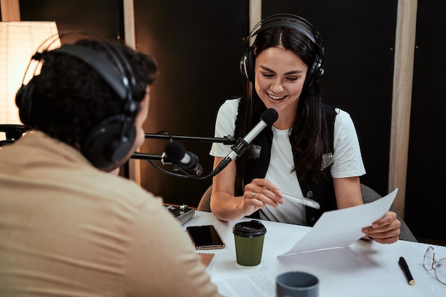 Portait of happy female radio host smiling reading a script from paper while talking to male guest