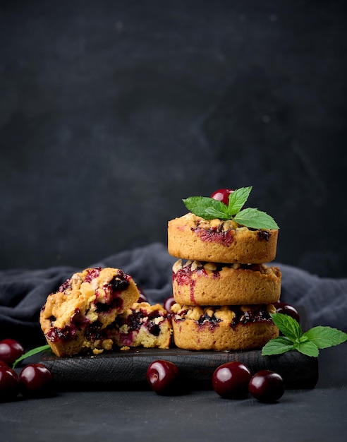 Portion crumble pie with cherries on a wooden board decorated with green mint leaves black background