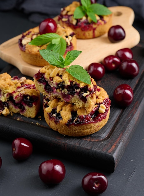 Portion crumble pie with cherries on a wooden board decorated with green mint leaves