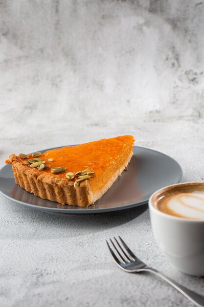 Portion of delicious bright orange pumpkin open pie on gray plate, decorated with pumpkin seeds with dessert forks close-up, top view. Bright marble background. Copy space. Vertical. menu for cafe