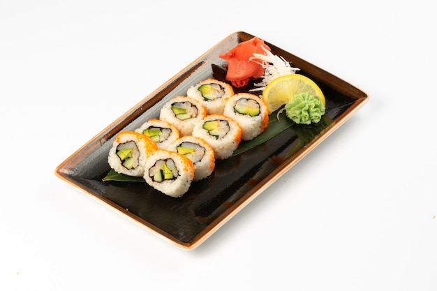 A portion of maki sushi with an assortment of Japanese side dishes in a rectangular ceramic plate on a white background