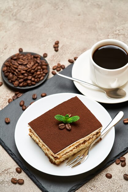 Portion of traditional italian tiramisu dessert and cup of coffee on grey concrete table