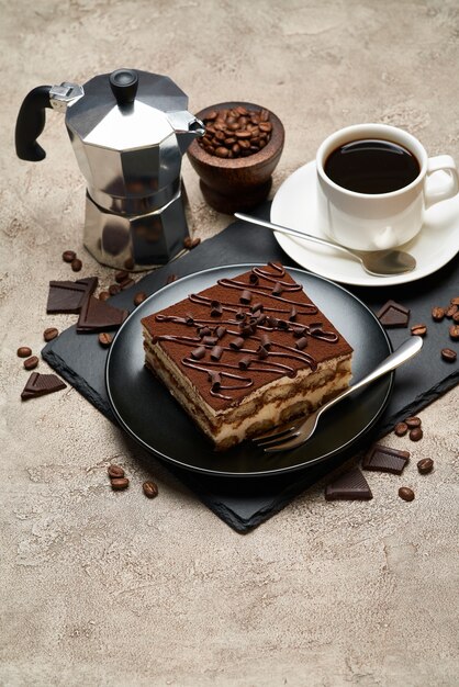 Portion of traditional italian tiramisu dessert and mocha coffee maker on grey concrete table