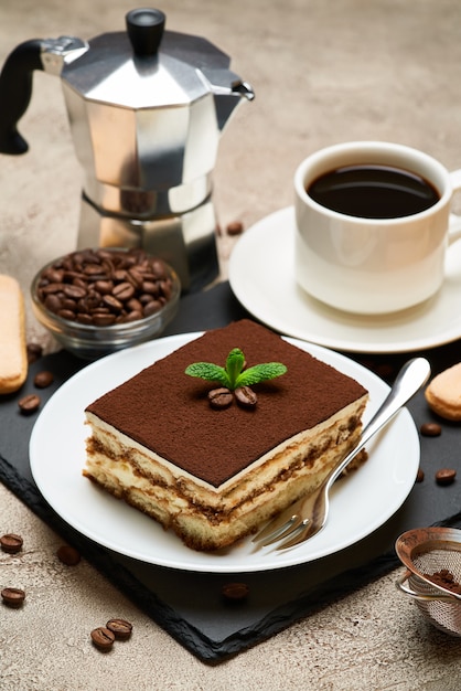 Portion of traditional italian tiramisu dessert and mocha coffee maker on grey concrete table