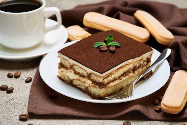 Portion of traditional italian tiramisu dessert and savoiardi cookies on grey concrete table