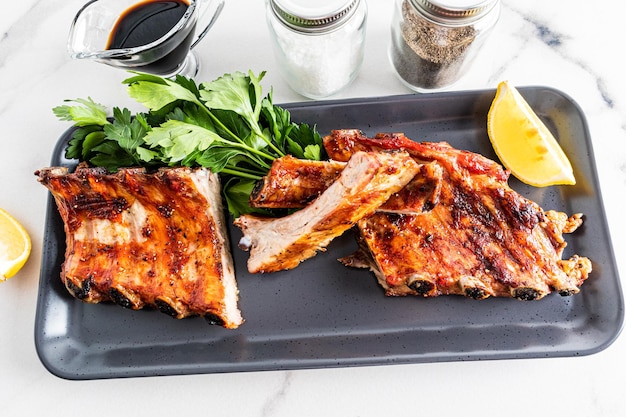 Portioned grilled pork ribs on a rectangular ceramic plate with parsley and lemon slice exquisite taste of food menu