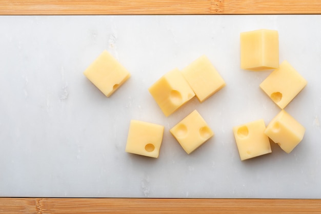 Portions (cubes, dice) of Emmental Swiss cheese . Texture of holes and alveoli. On white marble table.