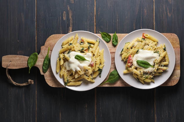 portions of pasta with tomatoes, spinach, parmesan and bolognese sauce on a large kitchen wooden board.