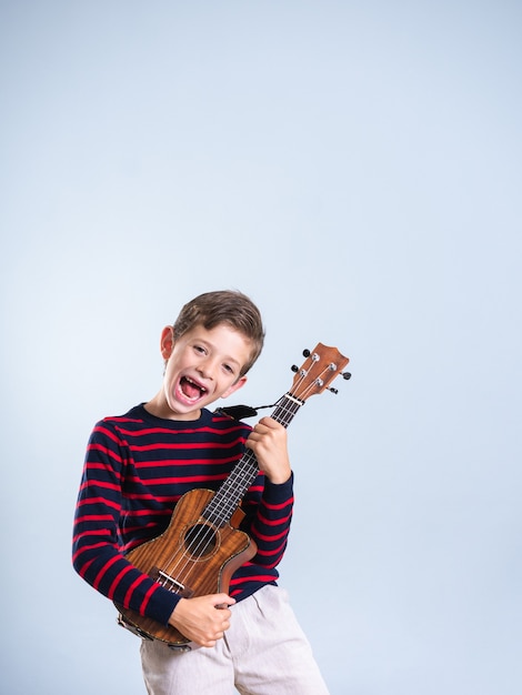 Portrait of a 7 year old boy playing the ukelele, isolated on a gray background