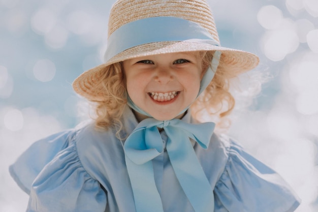 portrait of a adorable little blond girl in blue dress and straw hat outdoors