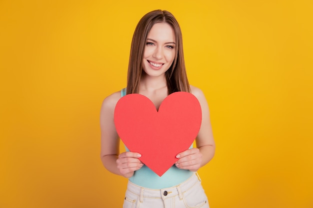 Portrait of adorable romantic lady hold demonstrate red paper heart card on yellow background