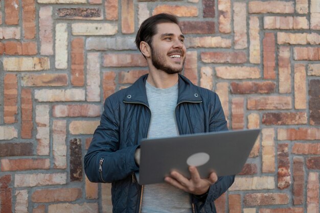 Portrait of an adult business man with a laptop in his hands against the background of a brick wall