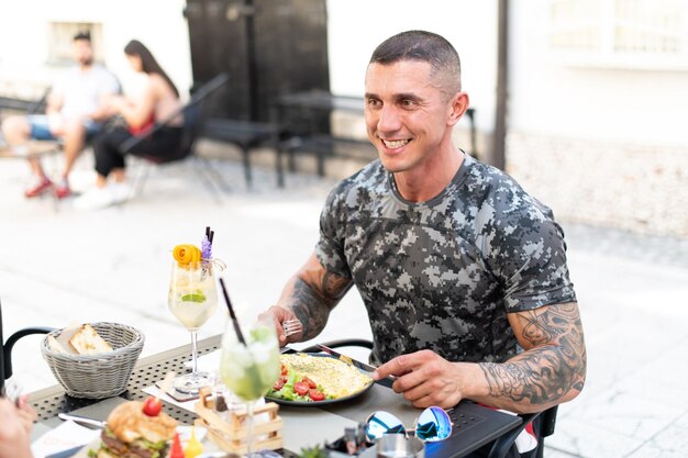 Portrait of Adult Man Eating Omelet or Scrambled Eggs Outdoors at Restaurant and Drinking Cocktail