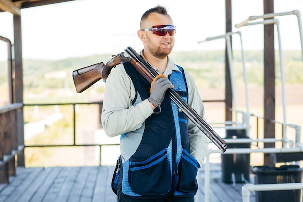 Portrait of adult smilling man in sunglasses protective headphones and a rifle vest