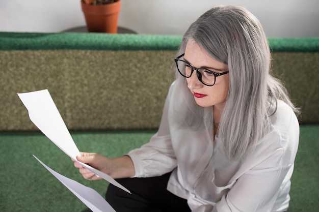 Portrait of an adult woman entrepreneur with grayish hair in a managerial position dressed in a white blouse and busy working in the office