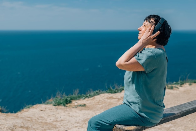 Portrait adult woman listens to music in headphones summer mountains enjoy pensioner