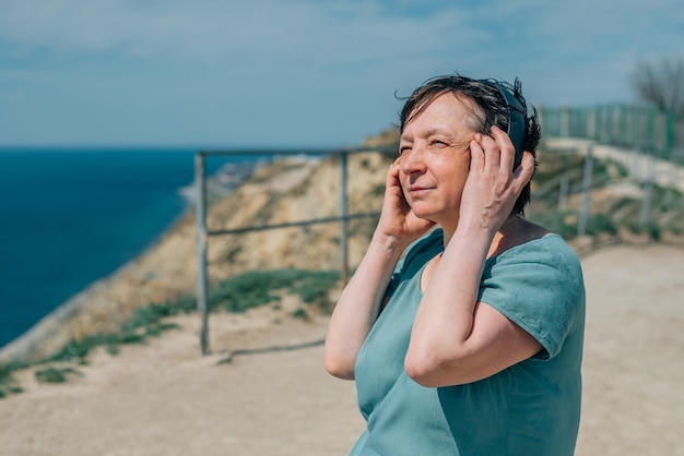 Portrait adult woman listens to music in headphones summer mountains enjoy pensioner