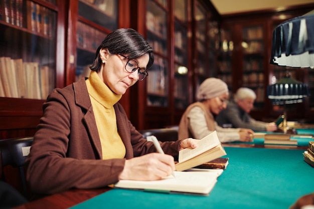 Portrait of adult woman studying in classic library interior by lamp light copy space