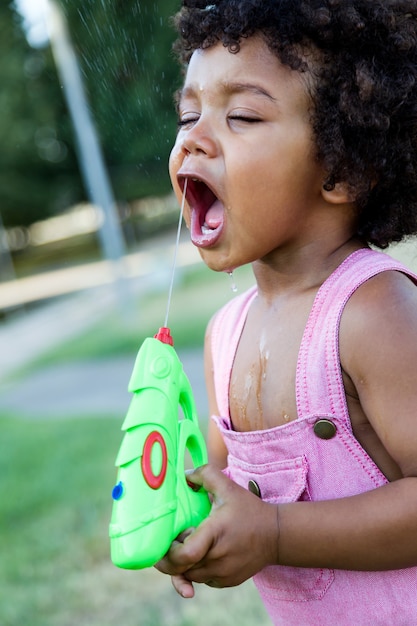 Portrait of a african american baby playing with water gun in the park.