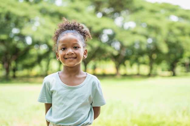 Portrait of African American little girl with curly hair smiling looking at camera in the park