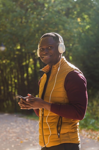 Portrait African american man listens music in autumn park background Gadget app and streaming service concept