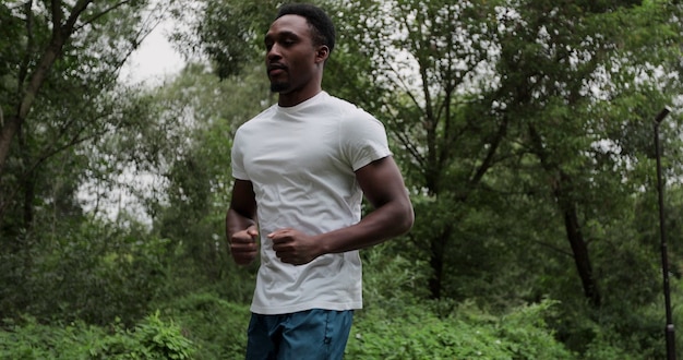 Portrait of african american runner man jogging in park. Male runner run in park at morning. Young man training run in slow motion. Cardio exercise at workout outdoor.