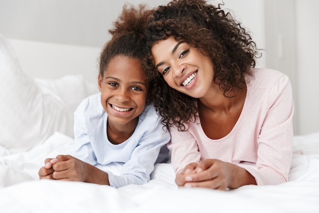 Portrait of african american woman and her little daughter smiling and lying in bed at home