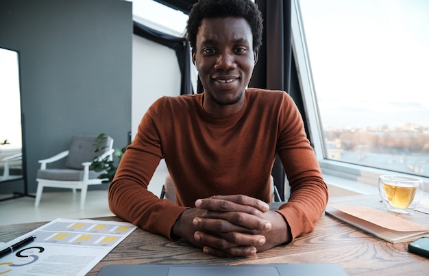 Portrait of African young man smiling at camera while sitting at his workplace at office