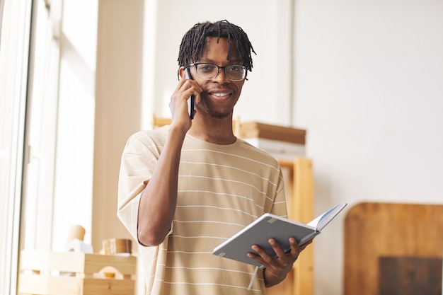 Portrait of African young man working on digital tablet and taking the order by the phone