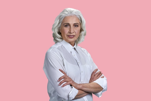 Portrait of aged senior lady with crossed arms isolated on pink background