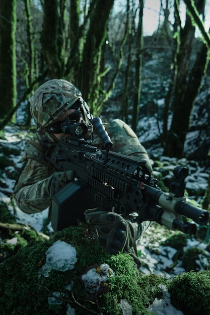 Portrait of airsoft player in professional equipment in helmet aiming at victim with gun in the forest. Soldier with weapons at war