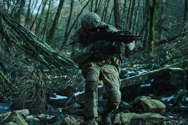 Portrait of airsoft player in professional equipment in helmet aiming at victim with gun in the forest. Soldier with weapons at war