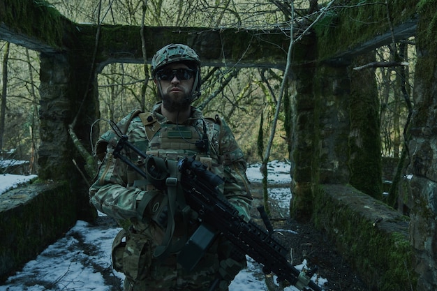 Portrait of airsoft player in professional equipment with machine gun in the forest. Soldier with weapons at war