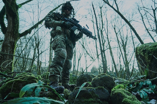 Portrait of airsoft player in professional equipment with machine gun in the forest. 