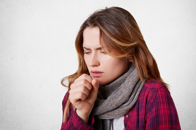 Portrait of allegic ill female has cough, caught cold, feels unhealthy, looks sick, wears warm knitted scarf on thore throat