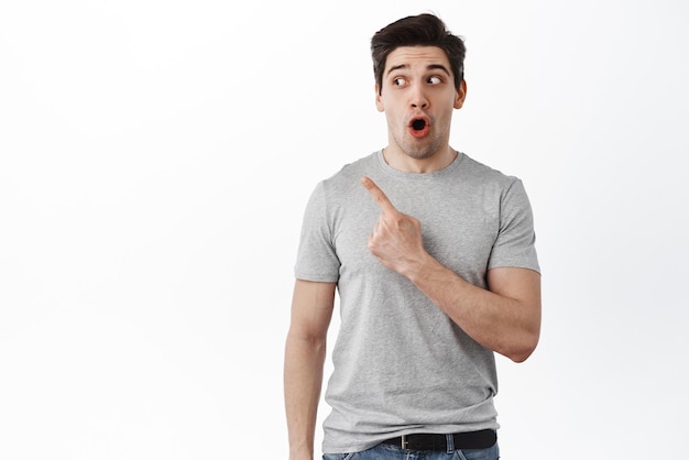 Portrait of amazed 30s guy say wow pointing and looking left at copy space with impressed face drop jaw from fascinating promo deal standing over white background