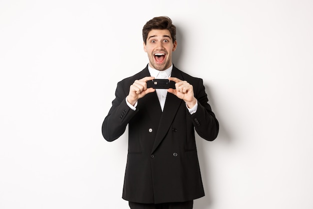 Portrait of amazed handsome man in black suit, showing credit card