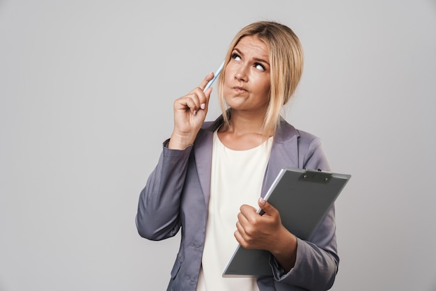 Portrait of an amazing thoughtful young pretty woman posing isolated over grey wall holding clipboard