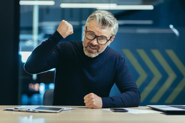 Portrait of an angry senior businessman sitting in the office in front of the camera and shouting