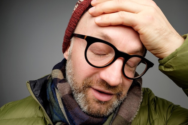 Portrait of annoyed tired handsome man with bristle leaning face on hand and looking indifferent down