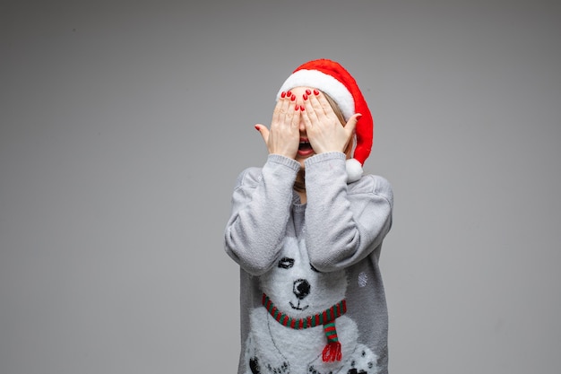 Portrait of anonymous fair-haired Caucasian woman with red nails wearing sweater with winter pattern hiding her eyes while laying on the floor with colorful confetti