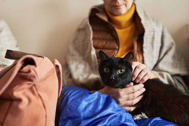 Portrait of anonymous senior woman holding loved pet cat in refugee shelter copy space