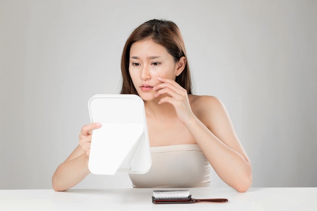 Portrait of ardent asian woman looking at mirror worry about pimple