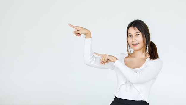 Portrait Asian beautiful woman wearing casual shirt standing poses, pointing advertisement on white background, blank copy space with an isolated smiling look at the camera.