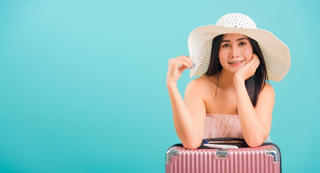 Portrait asian beautiful woman with hat her sitting with travel bag on weekends on blue background, with copy space for text