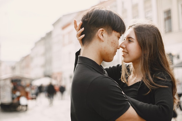 Portrait of an asian boy and his caucasian girlfriend in casual wear standing on  street. Couple is going to kiss each other while walking together in city.
Girl is touching his neck.