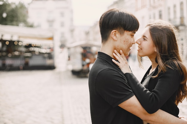 Portrait of an asian boy and his caucasian girlfriend in casual wear standing on  street. Couple is going to kiss each other while walking together in city